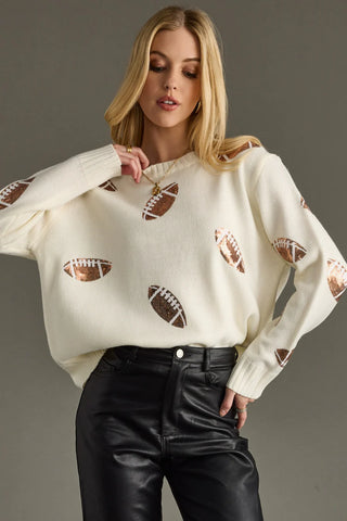 Woman wearing a white sweater with football cutouts on a gray background
