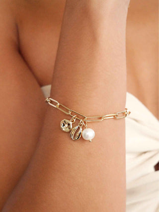 Gold bracelet with charms on a wrist against a neutral background