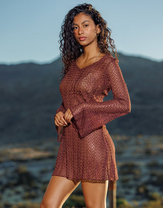Woman wearing a brown patterned dress standing against a mountainous landscape