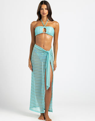 The model is wearing an aqua bandeau-style top with a halter tie and a keyhole cutout at the center, combining a chic and beach-ready design.