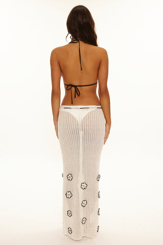 Woman wearing a black halter top and white pants with floral patterns on a white background