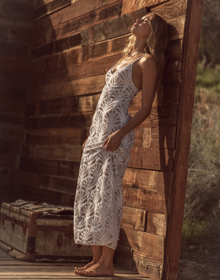 Woman in a white lace dress leaning against a wooden wall outdoors.