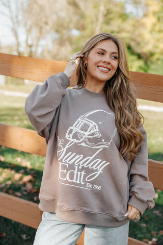 Woman wearing a gray sweatshirt with 'The Sunday Edit' logo outdoors.