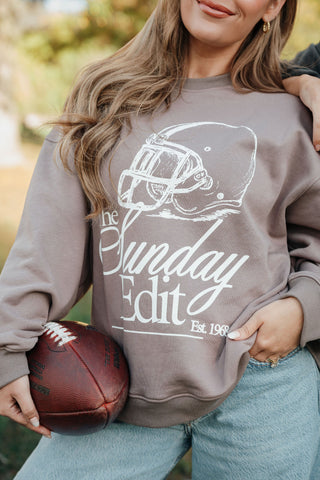 Person wearing a 'The Sunday Edit' sweatshirt holding a football outdoors