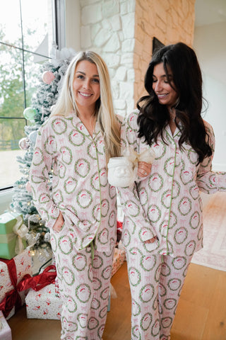 Two women wearing matching festive pajamas in a cozy room with a Christmas tree.
