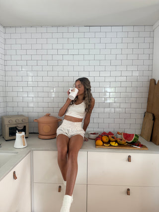 Woman wearing a beige tiger-print cropped tank top with a scoop neckline, sitting on a kitchen counter with white tile backsplash.