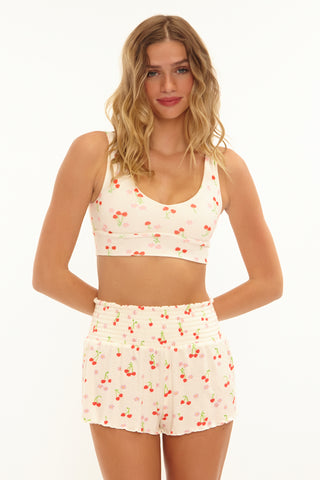 Woman wearing a matching cherry-patterned top and shorts set on a white background