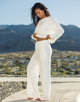 Woman in a white outfit standing in a desert landscape with mountains in the background