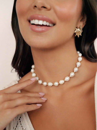 Woman wearing a pearl necklace and gold earrings with a blurred background