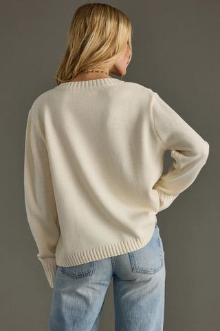 Person wearing a cream sweater and light blue jeans against a gray background