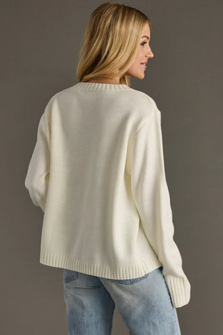 Woman wearing a cream sweater and blue jeans against a plain background