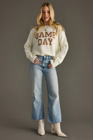 Woman wearing a 'GAME DAY' sweater and blue jeans against a gray background